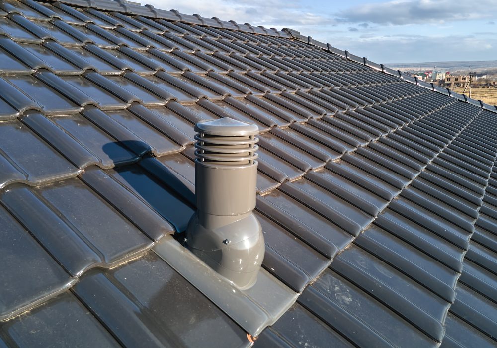 Closeup of ventilation pipe on house roof top covered with ceramic shingles. Tiled covering of building.