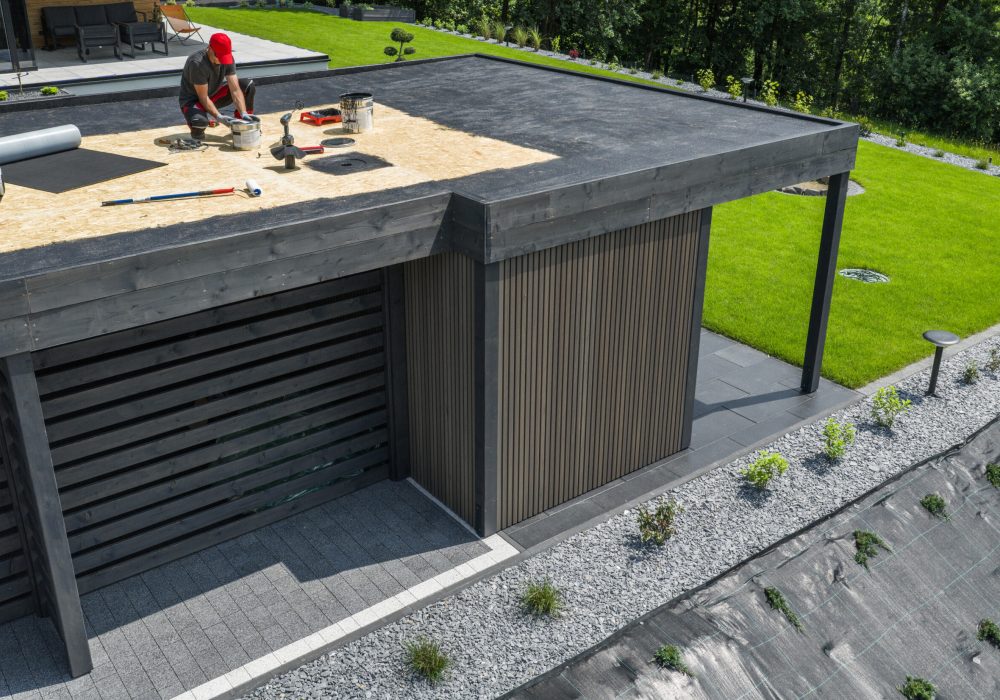 Skilled workers are completing maintenance tasks on the roof of a contemporary building, with lush greenery nearby and tools scattered around.